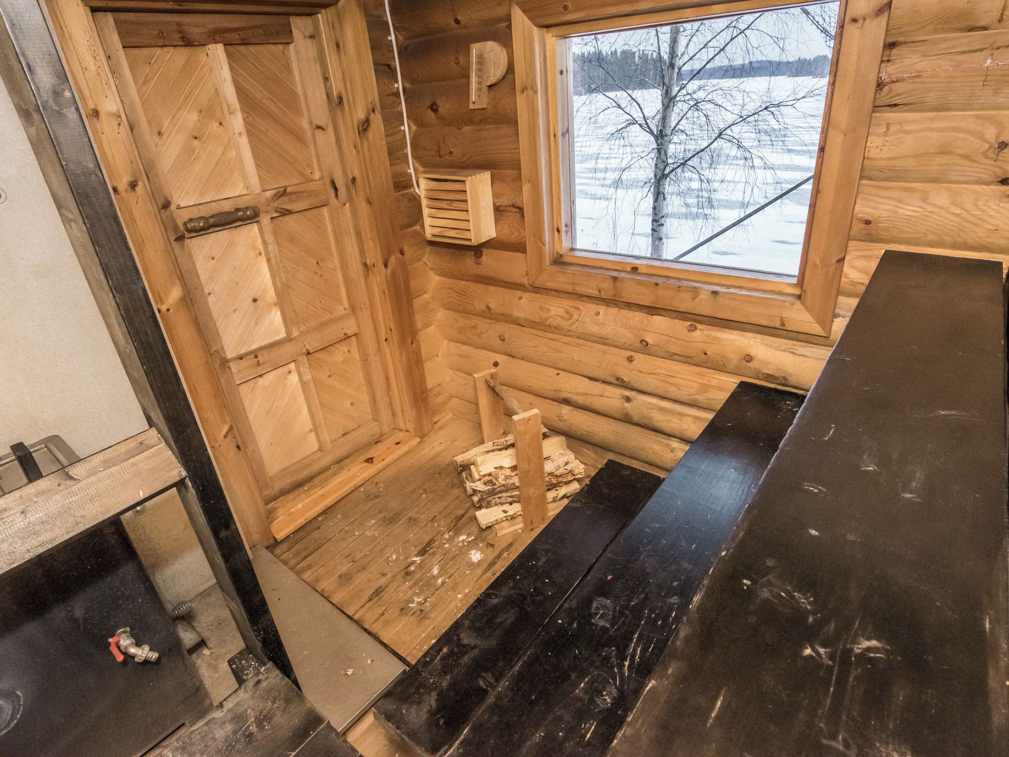 L’intérieur d’une cabane en rondins, avec une fenêtre, une cheminée et une porte en bois.
