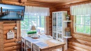 A cozy wooden cabin with a dining area, a television mounted on the wall, and a view of the outdoors.