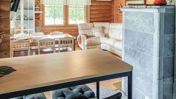 A wooden interior with a dining table, chairs, a sofa, and a stone fireplace.