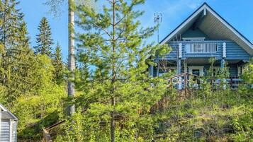 A log cabin with a balcony, surrounded by dense forest.