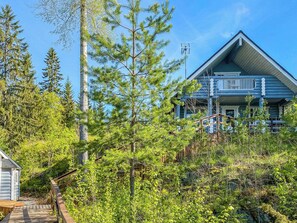 Une cabane en rondins dotée d’un balcon, entourée d’une forêt dense.