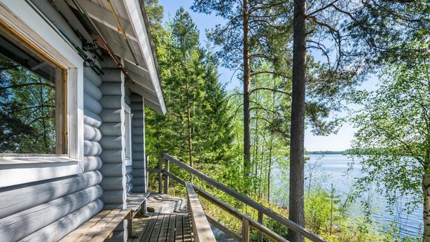 A wooden cabin with a deck overlooking a lake, surrounded by trees.