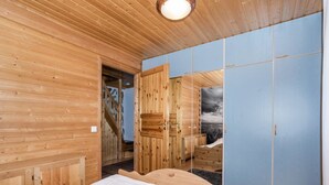 A wooden cabin bedroom with a bed, a wardrobe, and a door leading to a staircase.