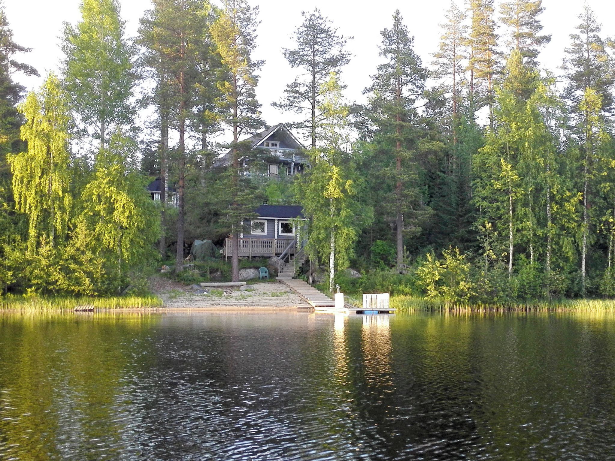 Una cabana a la vora d'un llac amb un moll, envoltada per un bosc dens.
