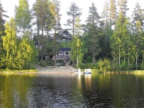 Una cabaña junto al lago con un muelle, rodeada de un bosque denso.