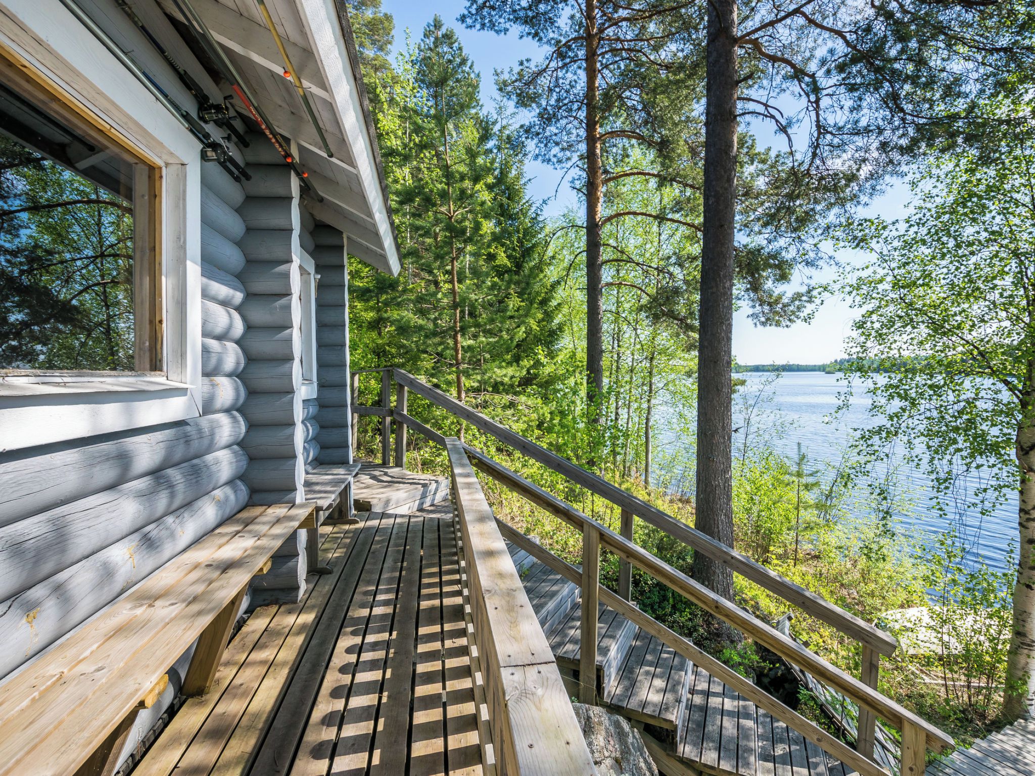 Een vakantiehuisje van hout met een houten terras, een bank en een leuning met uitzicht op een meer.