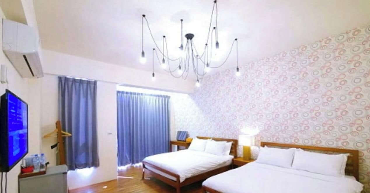 Habitación de hotel con cama, televisor, candelabro y pared con diseño.
