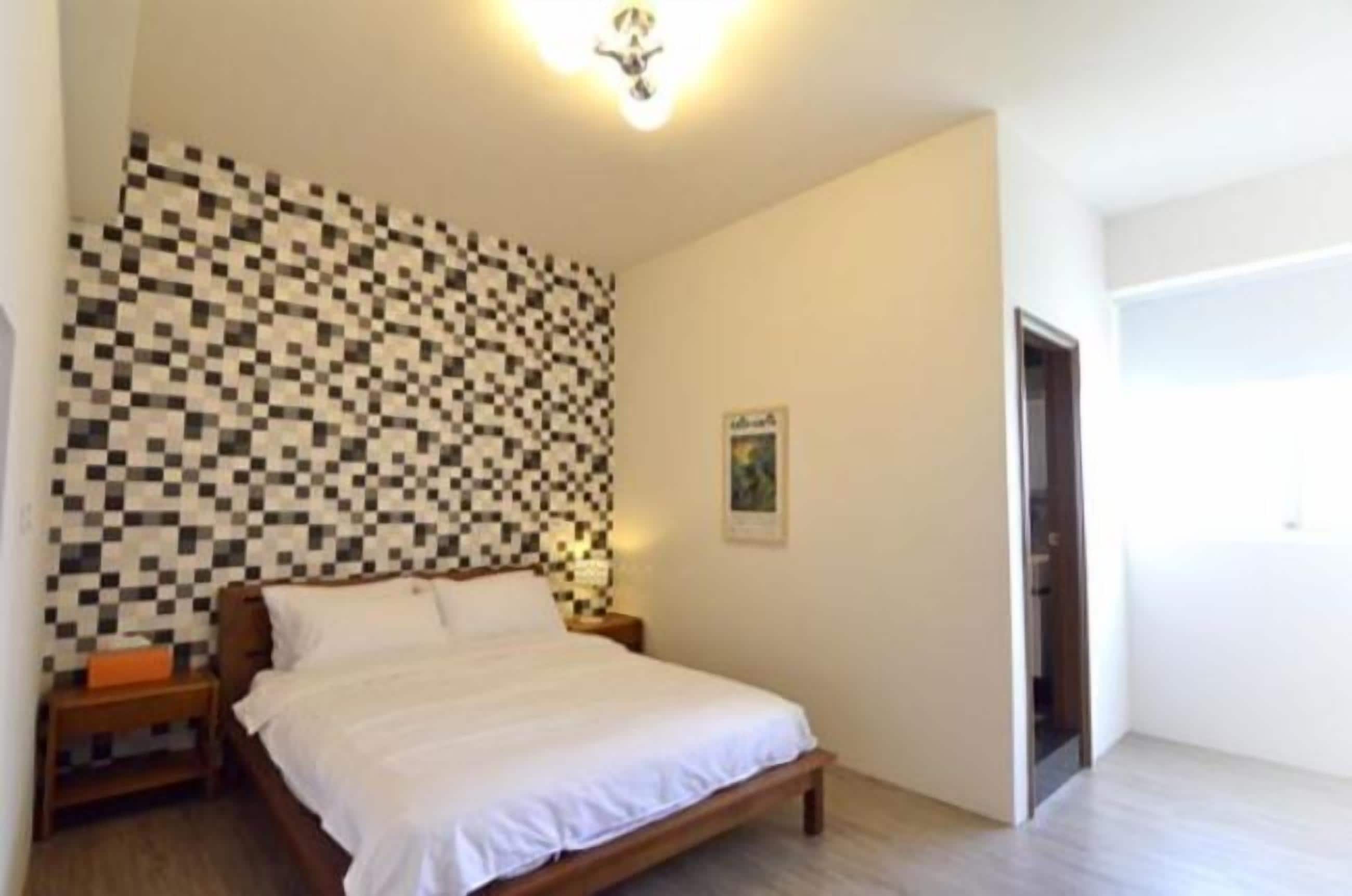 Une chambre avec un mur à carreaux, un lit, une table de chevet et une porte donnant sur une autre pièce.