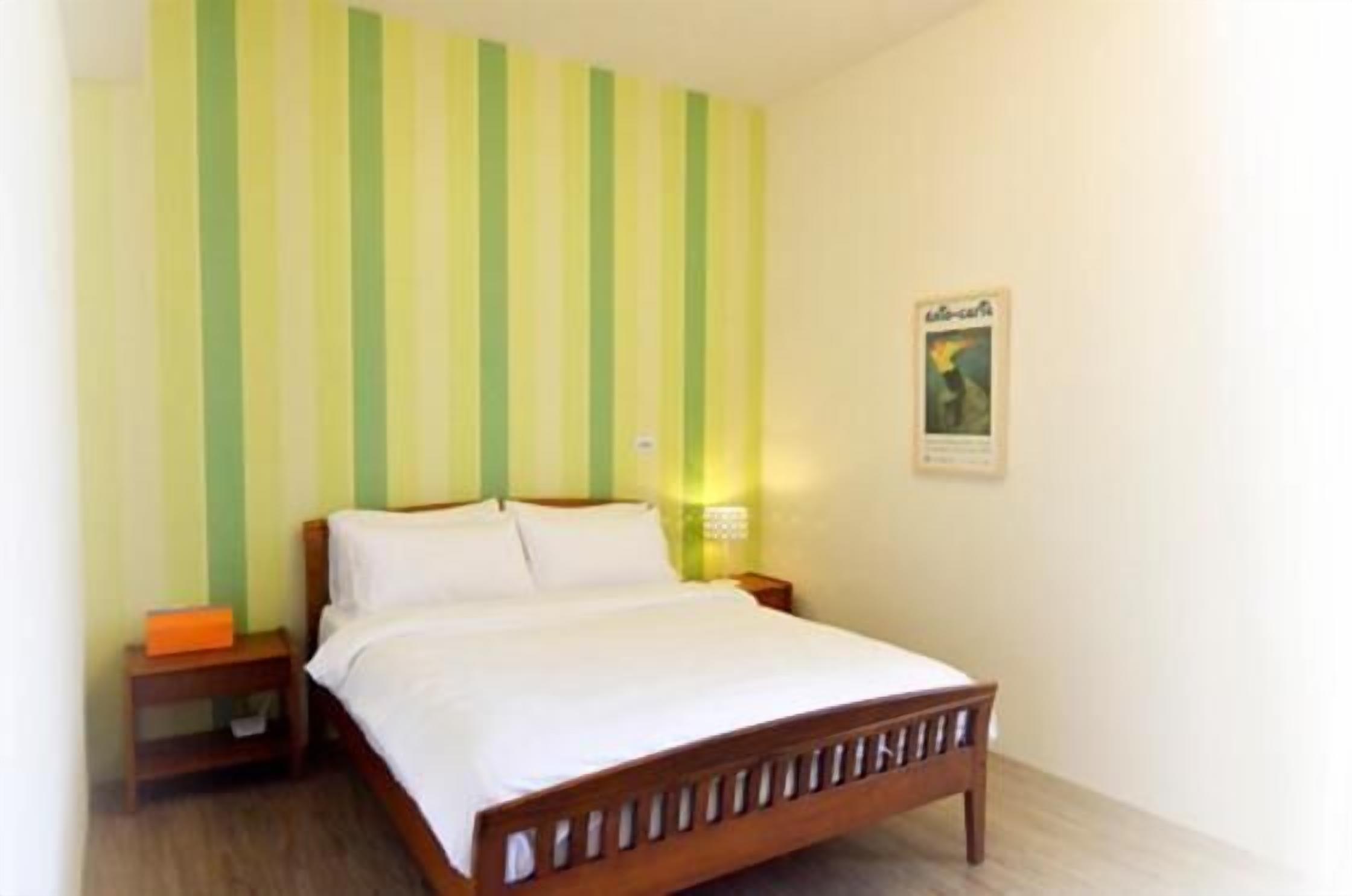 A single bed with a wooden frame, a nightstand with a lamp, and a striped wall.