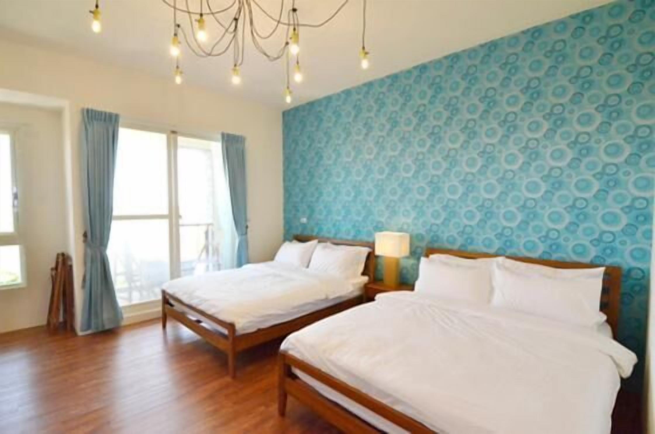 Een slaapkamer met twee houten bedden, een kroonluchter, een behang met patroon en een raam met gordijnen.