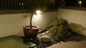 Un espace extérieur aménagé en jardin, bien éclairé, avec un arbre en pot, une petite fontaine et un jardin de rochers.