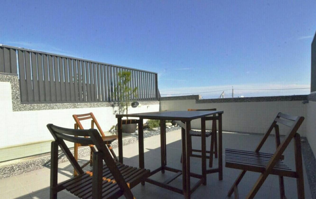 A patio with a table and chairs, a potted plant, and a view of the sea.