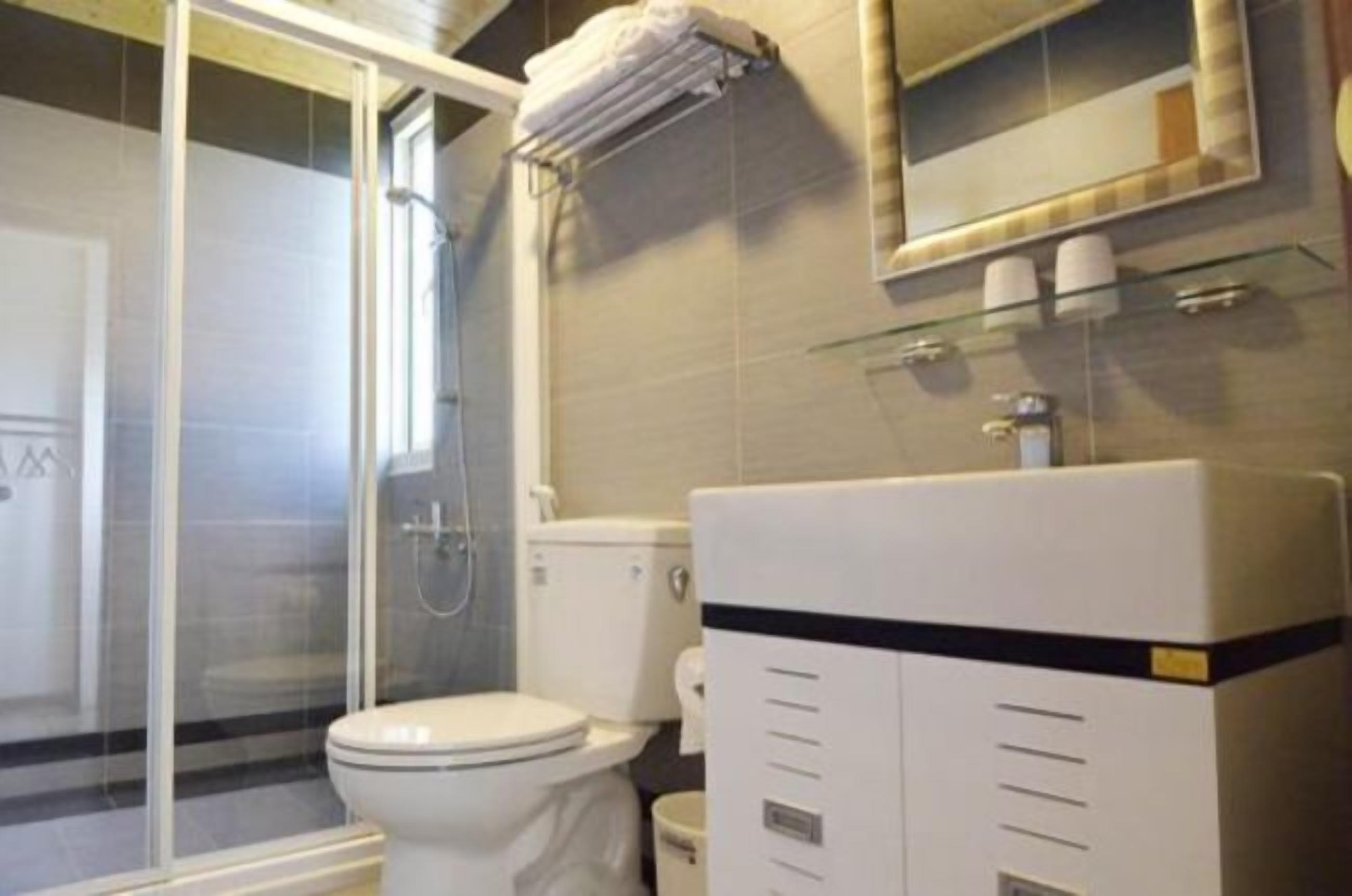 Un baño con cabina de ducha de vidrio, inodoro y lavamanos con espejo.