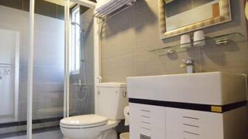 Un baño con cabina de ducha de vidrio, inodoro y lavamanos con espejo.