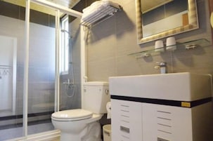 Un baño con cabina de ducha de vidrio, inodoro y lavamanos con espejo.