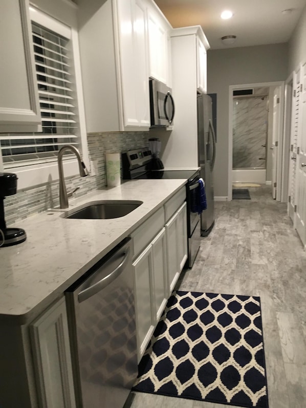A modern kitchen with white cabinets, a stainless steel sink, a built-in microwave, and a refrigerator.