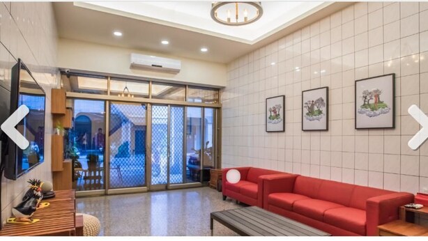 Un hall d’entrée avec un canapé rouge, un banc en bois et un téléviseur fixé au mur.