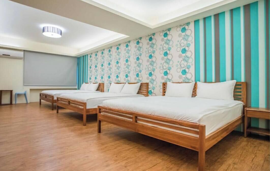 A hotel room with two wooden beds, a ceiling light, and a patterned wall.
