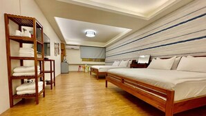 Une chambre d’hôtel avec un lit en bois, une étagère en bois où sont posées des serviettes, un petit bureau et un téléviseur.