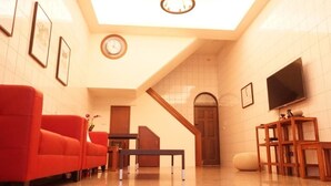 Un salon avec un canapé rouge, une table basse en bois, un téléviseur et un escalier menant à une autre pièce.