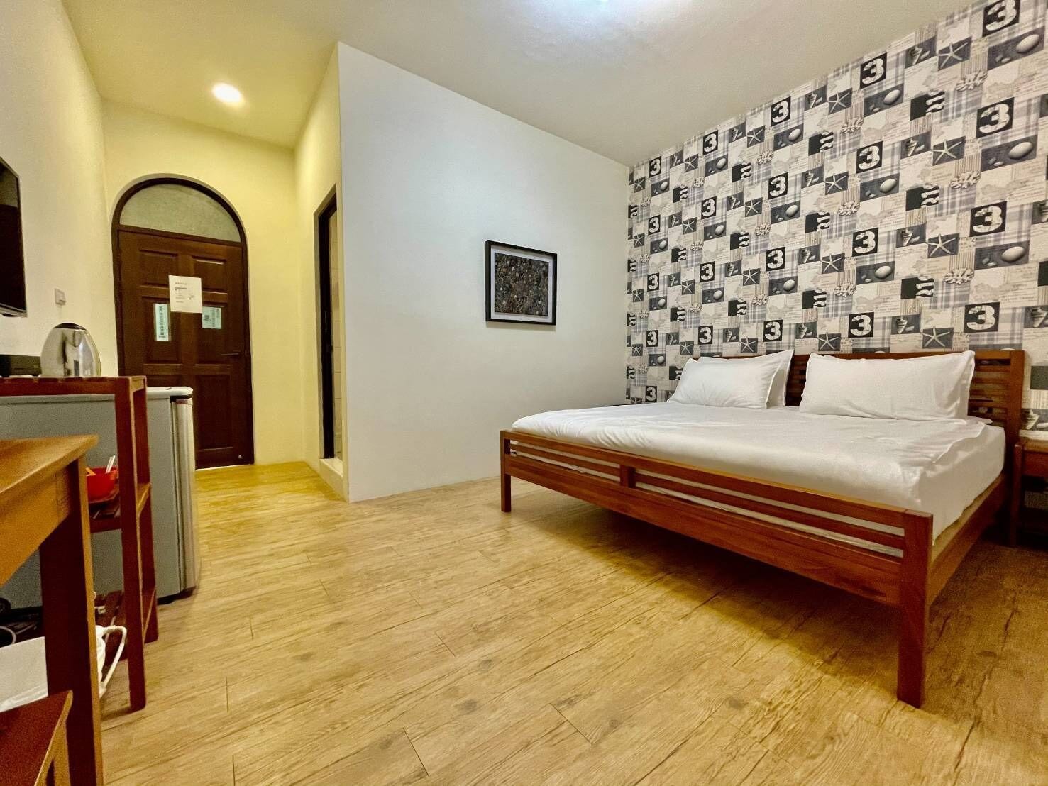 A bedroom with a wooden bed, a patterned wall, a door, and a small table with a kettle.