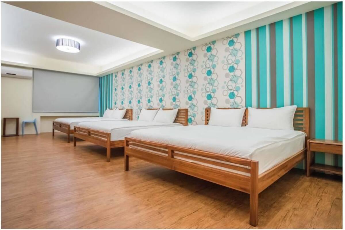 Une chambre d’hôtel avec deux lits en bois, une grande fenêtre et un mur à rayures.