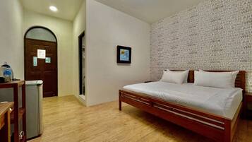 Un dormitorio con una cama de madera, un escritorio con silla, un pequeño cubo de basura y una puerta con un letrero.