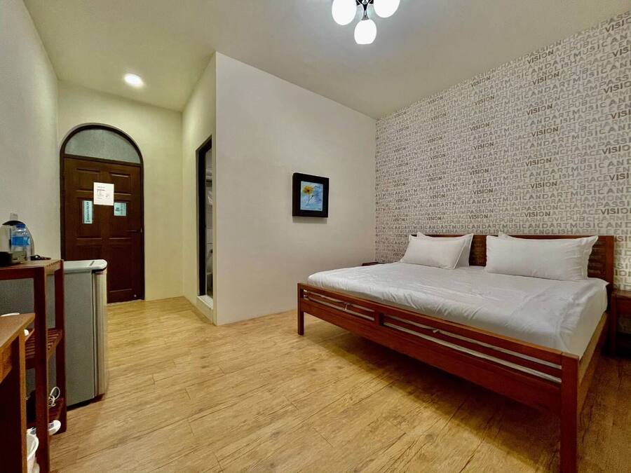 Un dormitorio con una cama de madera, un escritorio con silla, un pequeño cubo de basura y una puerta con un letrero.
