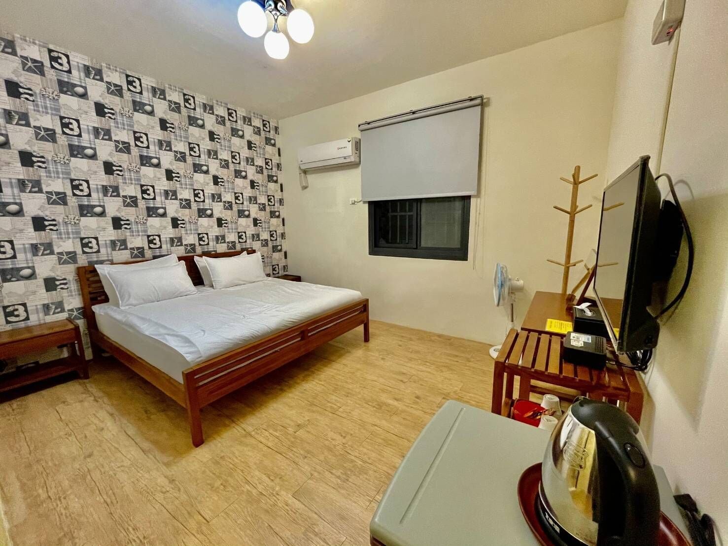 Een slaapkamer met een houten bed, een bureau met een computer, een ventilator en een televisie.