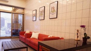 Un salon moderne avec un canapé rouge, une porte vitrée donnant sur l’extérieur et des œuvres d’art encadrées accrochées au mur.