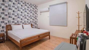A bedroom with a wooden bed, a white wall with a patterned wallpaper, a whiteboard, a coat rack, and a kettle.