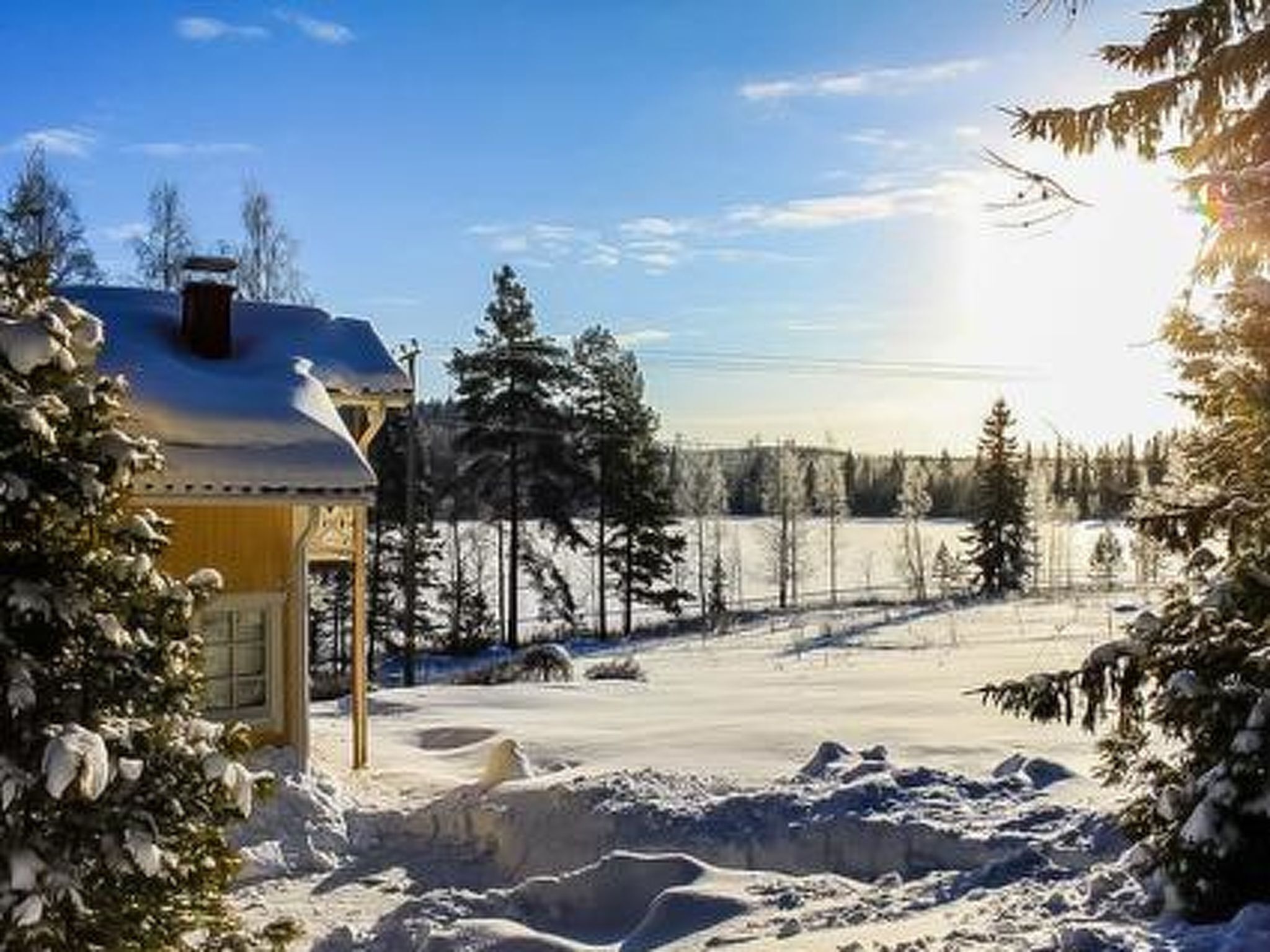 Een huis met een besneeuwde voortuin, een zichtbare schoorsteen en een heldere lucht.
