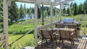 An outdoor wooden deck with a pergola, seating area, and a grill.