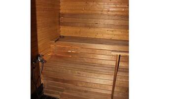 A wooden sauna room with a bench, a bench on the wall, and a metal door.