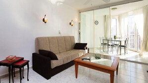 Un salon moderne avec un canapé, une table basse en verre et un coin repas visible à travers une cloison vitrée.