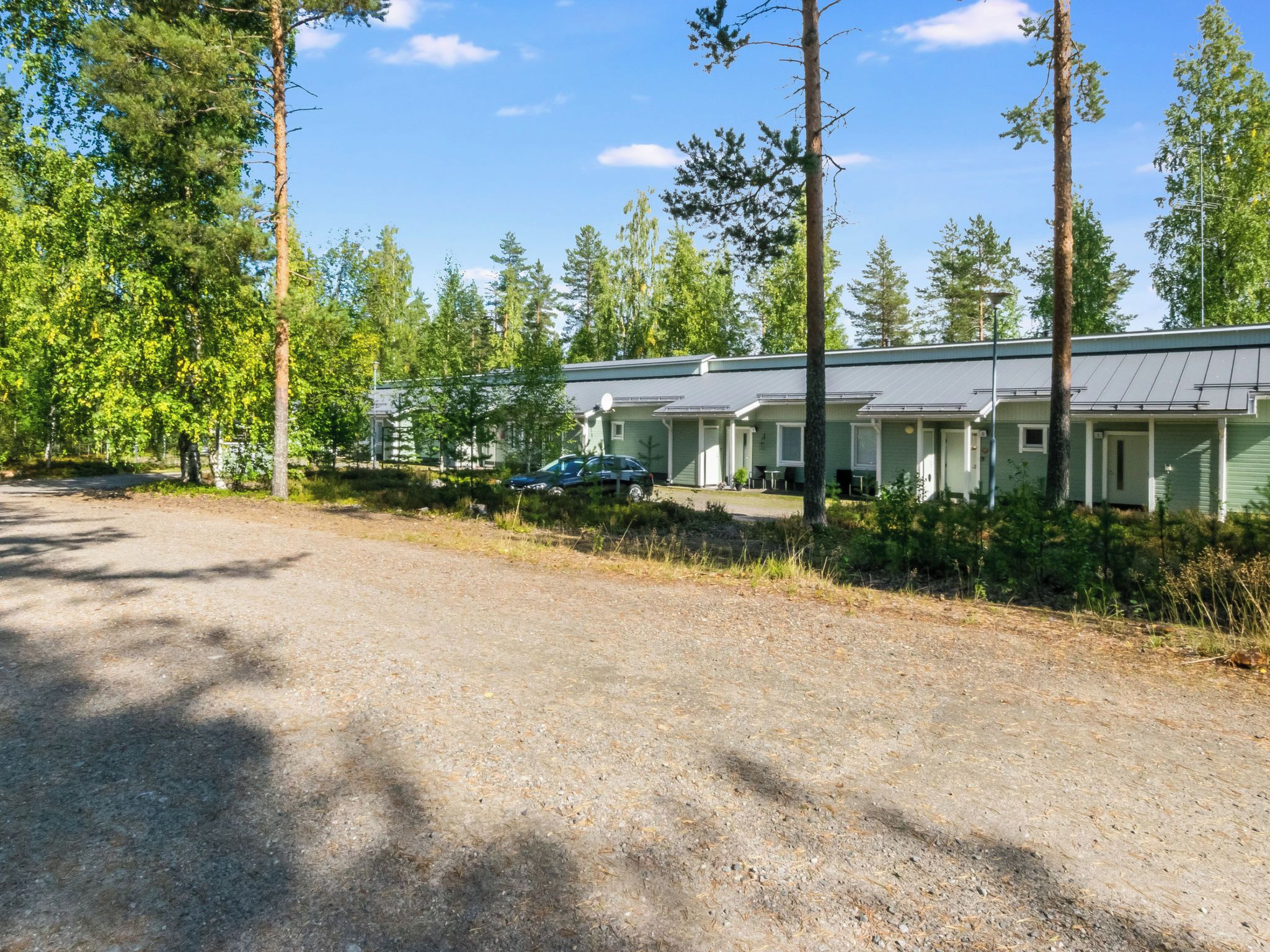 A row of single-story cabins with a gravel driveway, surrounded by trees.