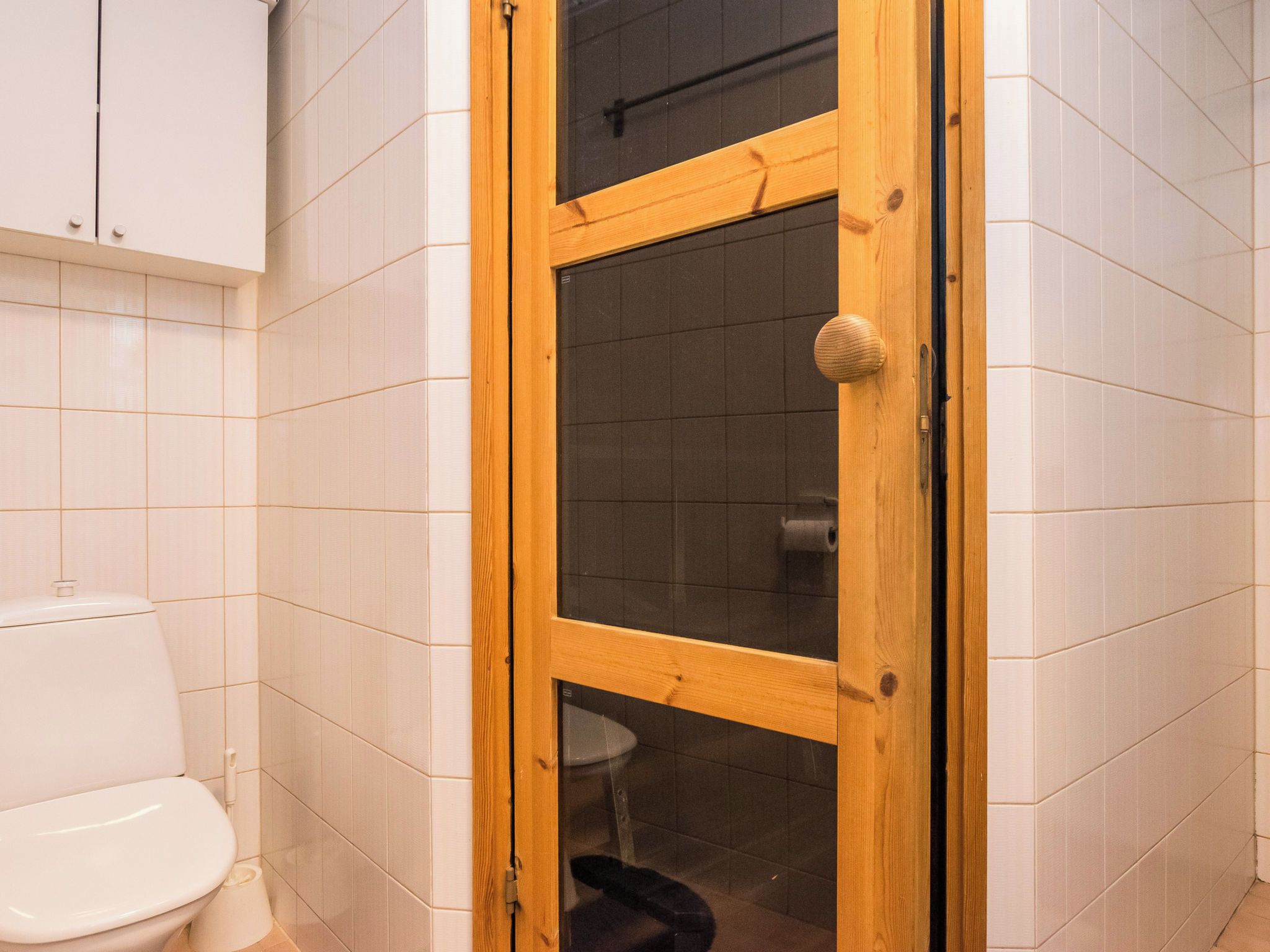 Une salle de bain avec une porte en bois, des carreaux blancs et des toilettes.