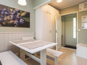 Quarto com uma mesa branca, bancos, pintura de amoras e uma porta que dá para outro aposento.