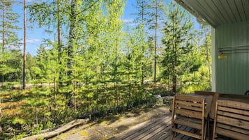Una terraza de madera con un banco, rodeada por un bosque de diversos árboles.