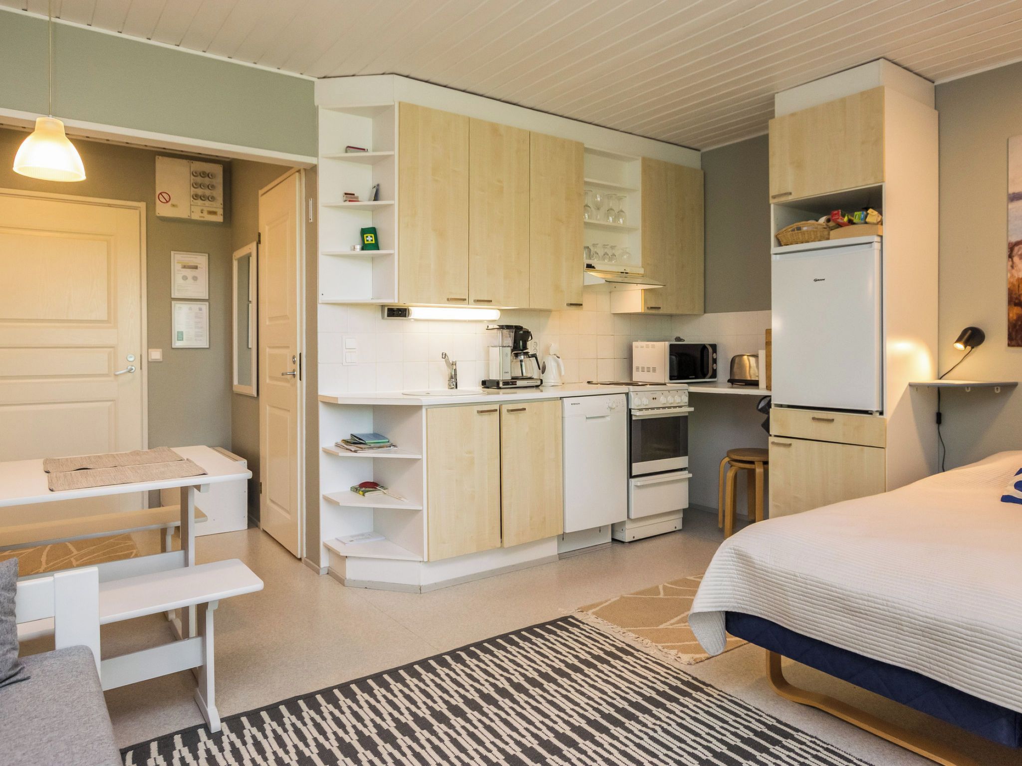 A compact bedroom with a bed, bedside table, and a small desk with a chair.