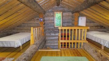 A log cabin with two bunk beds, a small table, a refrigerator, and a window with a view of greenery.