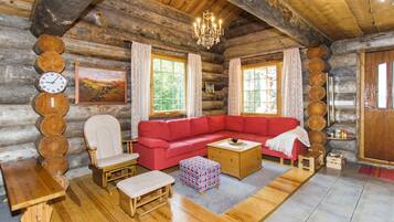 Interior d'una cabana de fusta amb un sofà vermell, mobles de fusta, un penjoll i un rellotge a la paret.