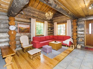 Interior de una cabaña de troncos con un sofá rojo, muebles de madera, una araña y un reloj en la pared.