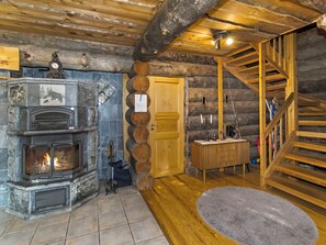 A log cabin interior with a stone fireplace, wooden staircase, and a small wooden cabinet.