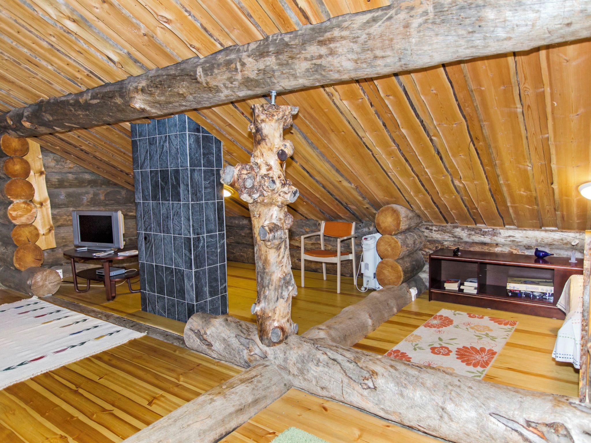 A rustic interior with wooden beams, a stone wall, a television, and a bookshelf.