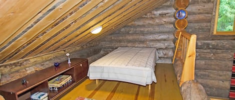 Een gezellig slaapkamer op zolder met een schuine kap, een houten bed, een klein bureau met boeken en een raam met uitzicht op groen.