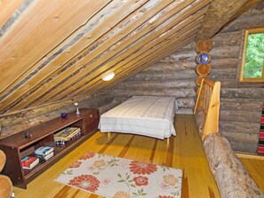 Une chambre mansardée chaleureuse, avec un plafond en pente, un lit en bois, un petit bureau avec des livres et une fenêtre donnant sur un paysage verdoyant.