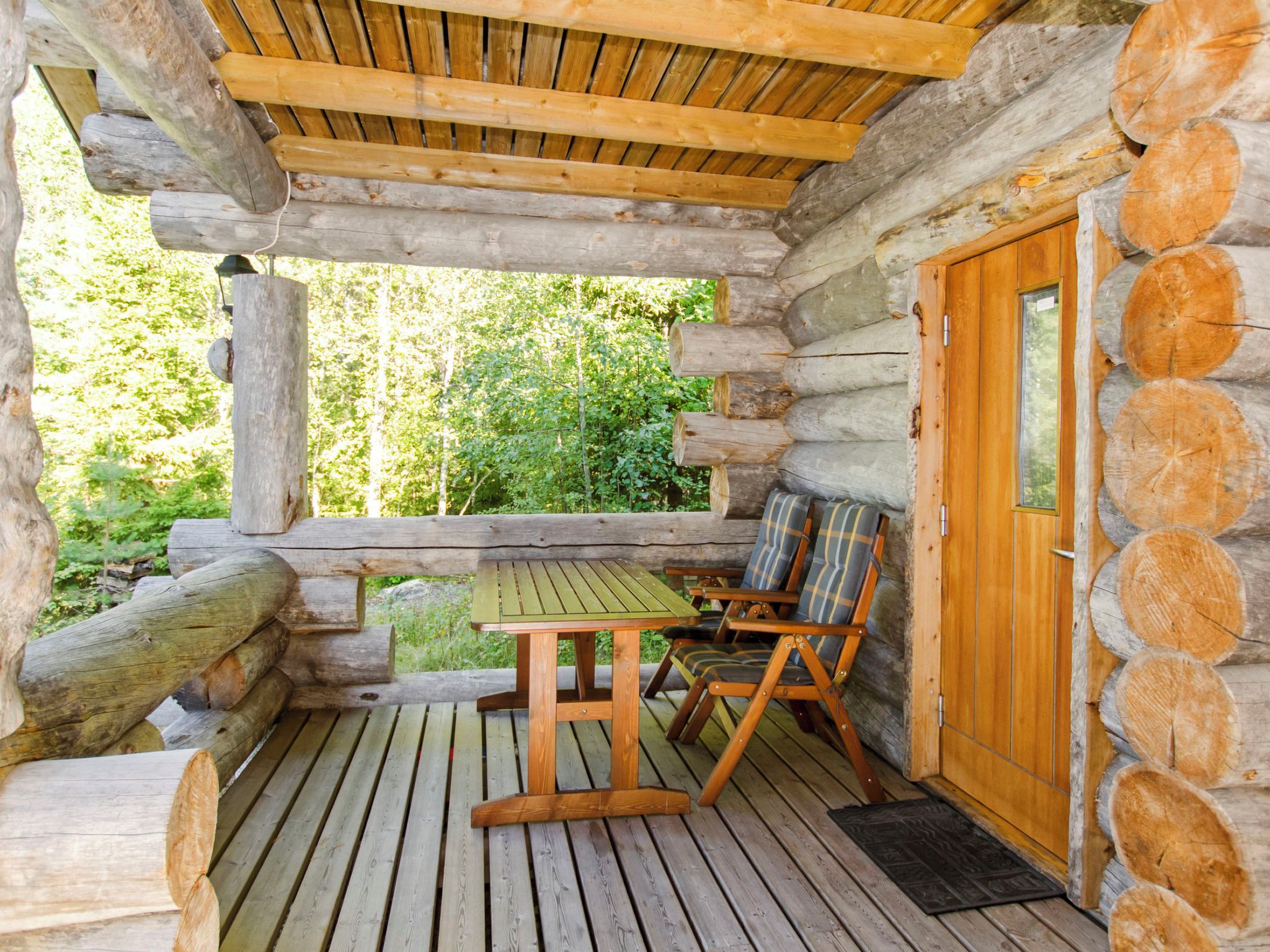 A log cabin with a wooden deck, a table, and two chairs.