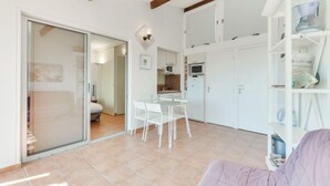 Een lichte, open woonkamer met een keuken, eethoek en een schuifglazen deur naar een andere kamer.