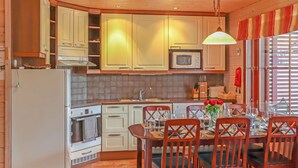 A kitchen with wooden cabinets, a refrigerator, a microwave, and a dining table set for four. - Villa hytönen 1 by Interhome (Äkäslompolo)
